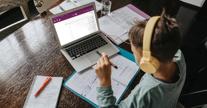 A young student is wearing headphones and participating in an online school lesson